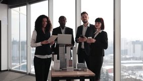 Team of diverse four multiethnic businesspeople having meeting in boardroom at office with panoramic windows blurry cityscape standing near table with skyscraper building maquette looking at camera - Powered by Shutterstock - Get 15% off with code: PIKWIZARD15