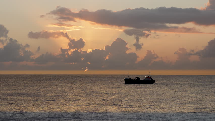 Cargo ship with excavator self-unloading system on the deck.  A magnificent sunset leaves the ship in silhouette at anchor