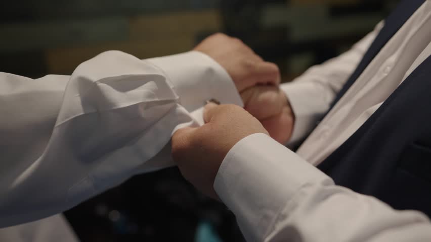 Groom preparing for the wedding. The best man helps him fasten the cufflinks on his white shirt. | Shutterstock HD Video #1100415513