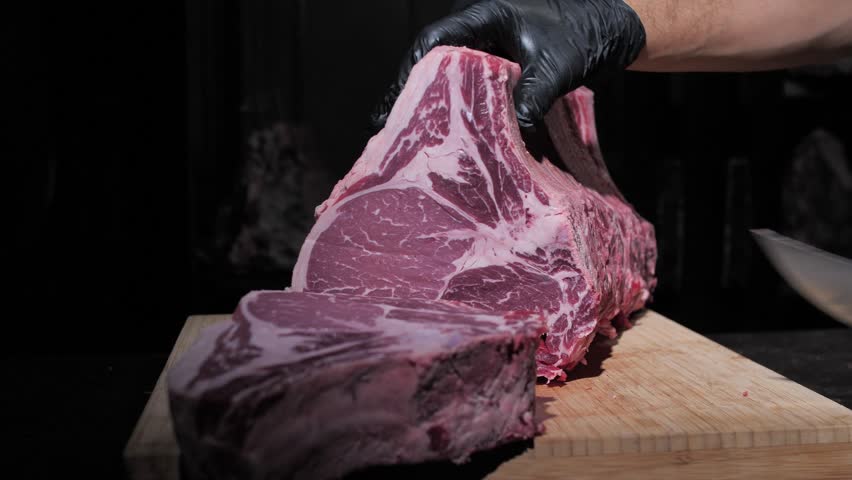 Professional chef puts piece of raw meat on wooden board and cuts for steak 