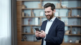 Smiling business man investor hold smartphone scrolling and watching social media at modern office workplace Happy bearded entrepreneur employer using phone app typing browsing on break indoors alone  - Powered by Shutterstock - Get 15% off with code: PIKWIZARD15