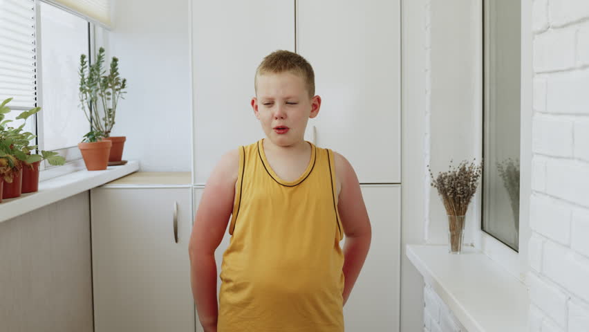 Portrait of crying and upset boy. Child stands on loggia and talks about insult, tears flow down his face. Boy wipes tears with hand. Kid in oversized yellow tank top with reddened sunburn on arms. Royalty-Free Stock Footage #1100422755