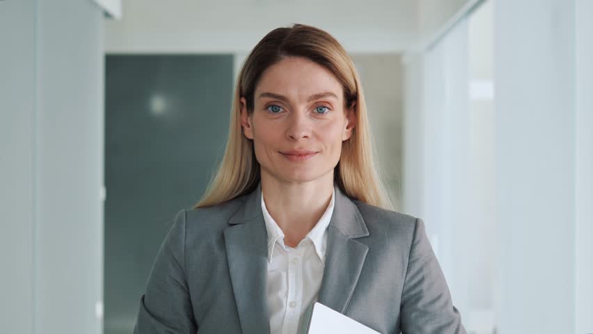 Portrait shot of beautiful Caucasian business woman looking to camera while smiling in office place. Adult entrepreneur, leader, manager posing in hallway. Close up face view business portrait. | Shutterstock HD Video #1100422829
