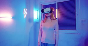 Gamer in VR headset glasses exploring metaverse plays online video game touching something on air with neon lights, Excited woman playing watching video life simulation at home