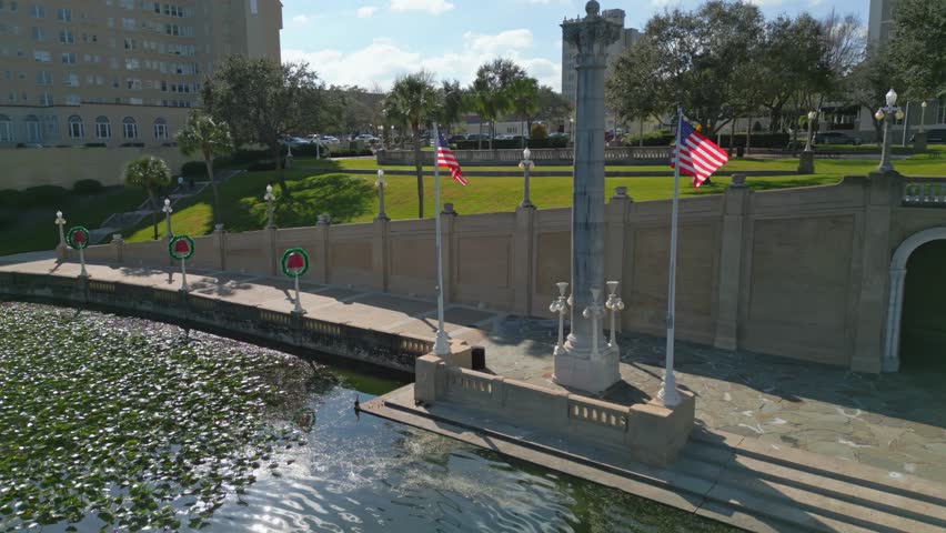 American flags stand tall above Lake Mirror in the centre of Lakeland, Florida. Aerial pan right. 