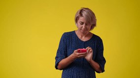 4k video of one woman typing text on the phone and looking around over yellow background.