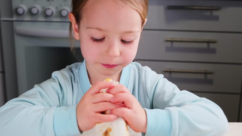 little girl child eating big fast food home made enjoys the taste at kitchen