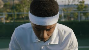 Portrait of young black man in headband with tennis racquet while playing at sports court