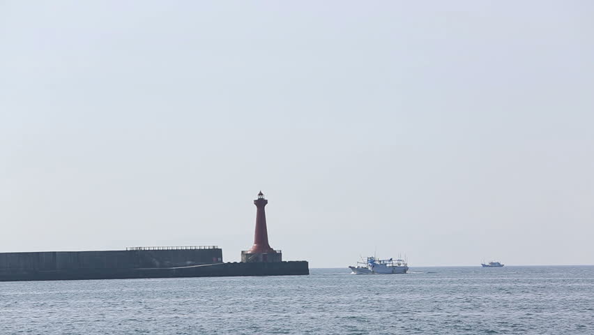 boat sailing under guide of the lighthouse in the sunset