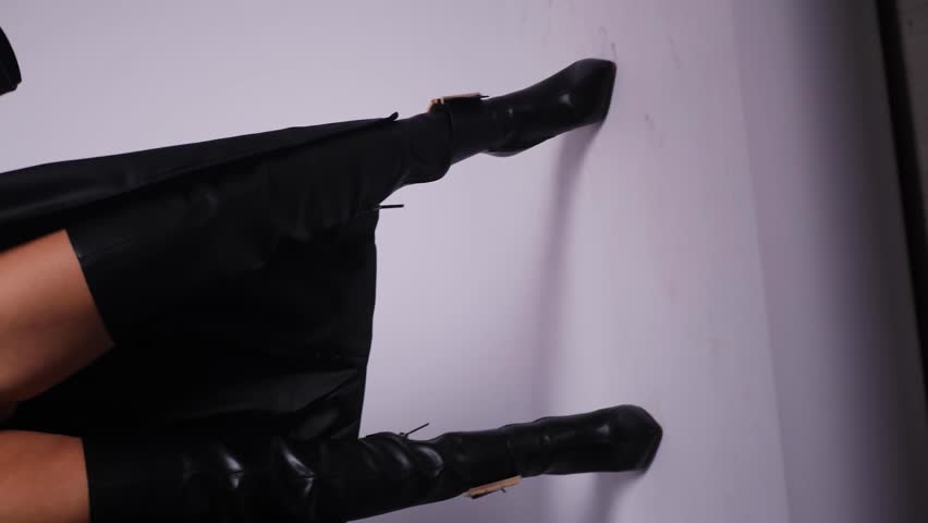 sexy young fashionable woman model in a black swimsuit and leather boots and coat is dancing in the studio on a white background. Vertical