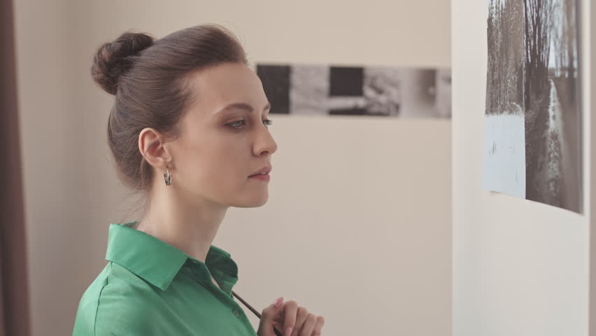 Chest up slowmo of young elegant Caucasian woman looking at black and white photos on walls visiting modern art gallery