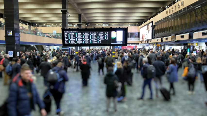 Train station concourse with moving camera showing information boards and people. Wide angle. People blurred for anonymity. Royalty-Free Stock Footage #1100445521