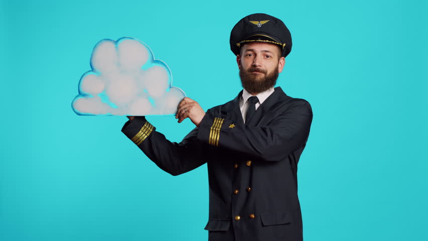 Male aviator playing with airplane toy and cloud board, holding cardboard icon and small miniature aircraft on camera. Young flying pilot with aviation uniform advertising aerial transport.