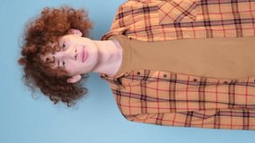 Vertical video. Curly positive student on beautiful blue background posing and gesturing with hands