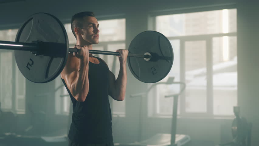 Portrait of caucasian sportsman lifting heavy weights in gym studio. Close-up view of a focused athlete in black sportswear performing barbell curls exercises. High quality 4k footage Royalty-Free Stock Footage #1100447913