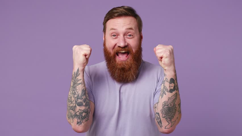 Excited jubilant overjoyed happy fun exultant young man 30s wear casual clothes doing winner gesture celebrate clenching fists say yes isolated on plain pastel light purple background studio portrait