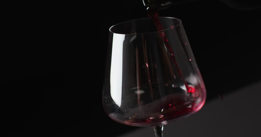 Red wine pouring into glass on black background with copy space. Wine, alcohol, beverage and wine tasting concept.