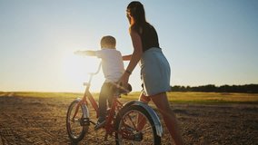 mom teaches son to ride a bike. happy family childhood dream concept. mom and little son learn to ride a bike silhouette in the park in nature. sunlight happy family goes in for sports outdoors - Powered by Shutterstock - Get 15% off with code: PIKWIZARD15