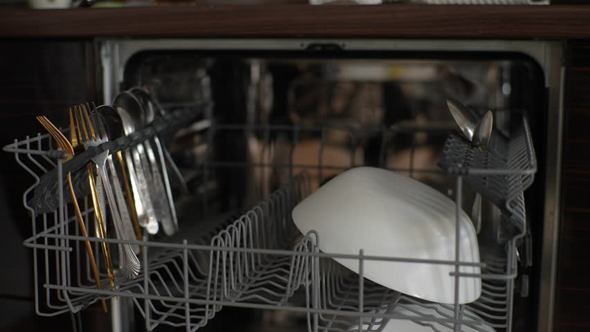 Close-up cropped shot of unrecognizable male loading dishwasher with dirty spoons. Man putting dirty stainless cutlery in dishwasher. Guy using modern appliance to keep home clean, slow motion. | Shutterstock HD Video #1100453229