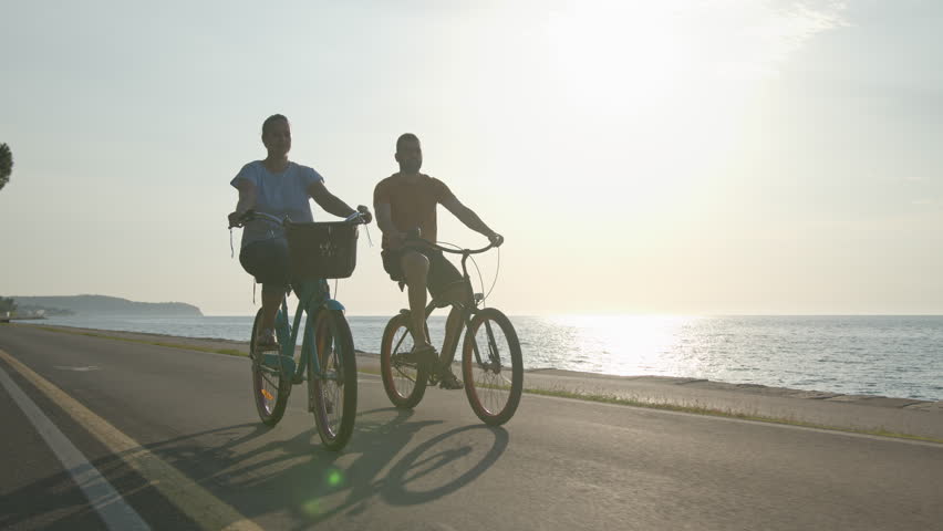 Caucasian couple taking pleasure in the ride on beach cruiser bikes, pedaling on a wonderful route near the sea, handheld shot. Royalty-Free Stock Footage #1100454693