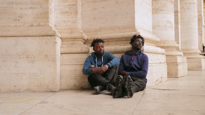 hardship, poverty - young migrants sitting on the ground with sad eyes
