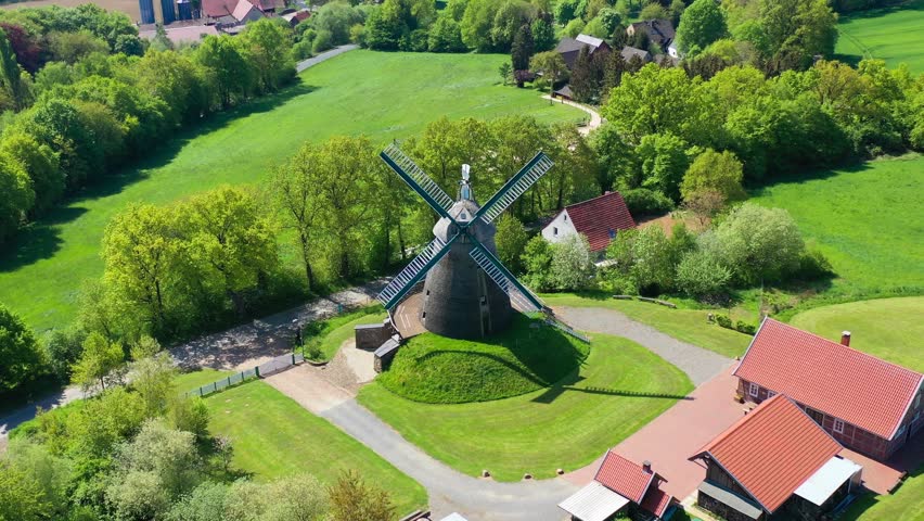 Summer aerial drone view landscape old windmill. Blooming rapeseed agricultural fields on background and farmers houses in Germany countryside. High quality 4k footage