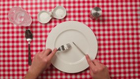 Top view of an unrecognizable man eating invisible food using cutlery in an empty plate. Male hands with knife fork cut invisible food in an empty clean white plate. Overeating control concept. - Powered by Shutterstock - Get 15% off with code: PIKWIZARD15