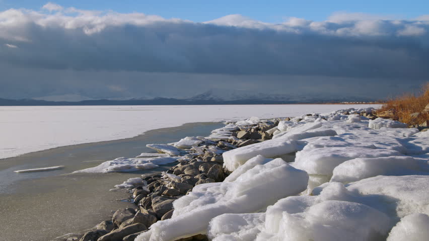 Looking over ice piled on the shoreline of Utah Lake in time-lapse as clouds move on the horizon during winter.