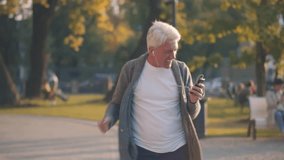 Optimistic happy senior man in earphones enjoying song on phone dancing at autumn park. Cheerful mature man in headphones listen to music and dance outdoors. Realtime - Powered by Shutterstock - Get 15% off with code: PIKWIZARD15