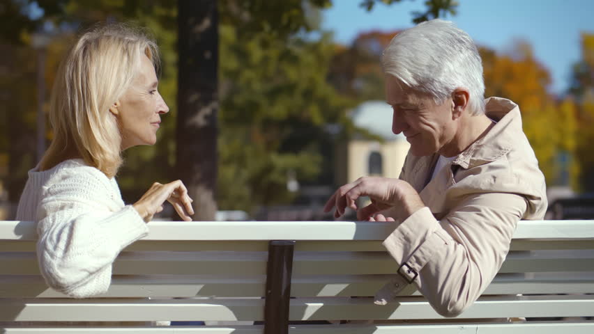 Side view of senior couple hold hands outdoors. Mature man and woman holding hands on date in park. Romantic aged couple hold hands sitting on bench in city. Realtime  | Shutterstock HD Video #1100464923