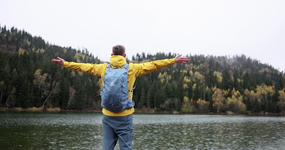 Traveler stands and raises hands in mountain lake