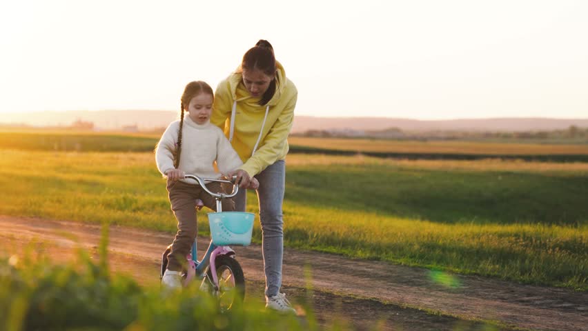 Mother teaches child ride two-wheeled bicycle sunset. fun weekend by bike. child's dream kid. child drive bicycle. mom rides girl child daughter bikerays sunset. happy family concept. teamwork. | Shutterstock HD Video #1100468443