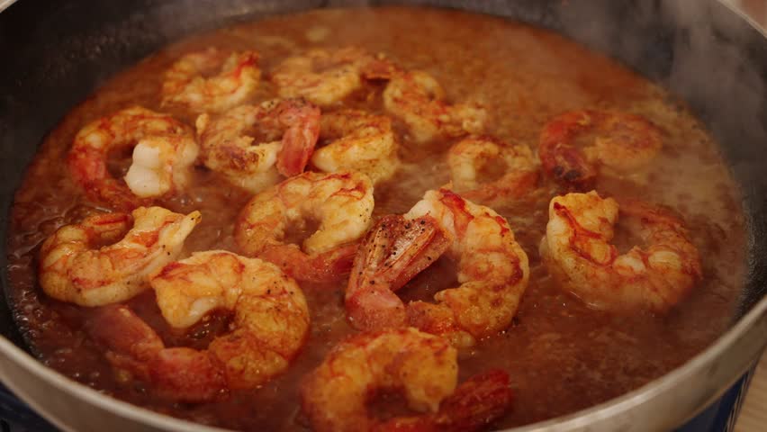 Delicious peeled shrimps simmering and boiling on hot pan, reducing and absorbing juicy flavours of red paprika spice with aromatic smokes flowing in the atmosphere, cooking seafood cuisine. Royalty-Free Stock Footage #1100470773