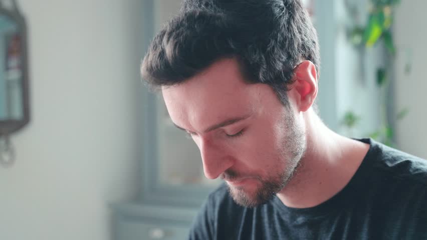 Young caucasian man bites into burger at home, cheeseburger eating enjoyment, close up portrait fast food eating, unhealthy eating concept obesity