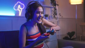 Young asian woman playing game online at home. Gamer controlling joystick for video game. Teenage girls leisure game in neon light room at home.