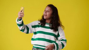 4k video of one young girl makes a video on her phone and showing thumbs up over yellow background.