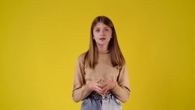4k slow motion video of one girl who smiles sweetly and puts his hands to his cheeks over yellow background.