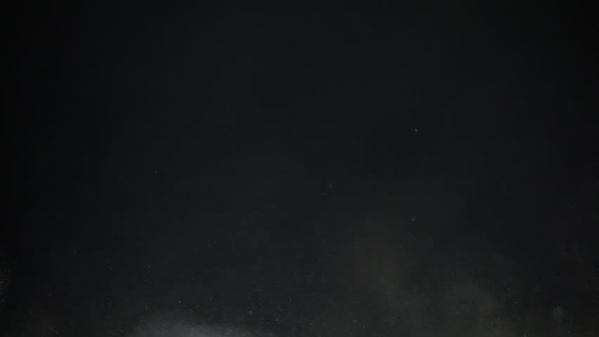 Turbulence dust particles rise into the air on a black background in slow motion
