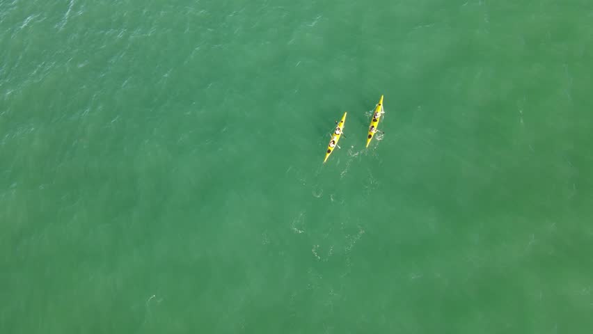 Two yellow kayaks paddling on green ocean waters of Atlantic Ocean, Uruguay. Aerial top-down forward directly above and slow-motion