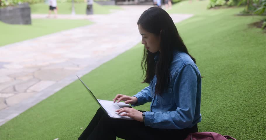 Portrait of a cute asian student girl coding IT laptop outdoors on grass in an open mall outside