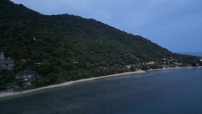 Aerial video of the beach strip in the evening, Ko Pha Ngan Island, Thailand, with a village and small fishing boats in the background