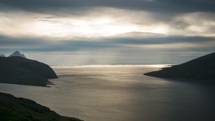 Time lapse of moving clouds and sun breaking through captured high above fjord in Norway towards the ocean
