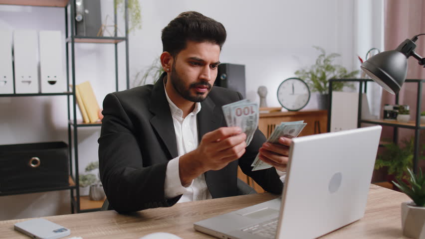 Rich indian businessman working on laptop pc counting money cash, calculate earnings income profit at home office workplace. Professional manager freelancer man. Business people. Employment occupation | Shutterstock HD Video #1100486801