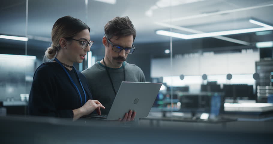 Portrait of Two Creative Young Female and Male Engineers Using Laptop Computer to Analyze and Discuss How to Proceed with the Artificial Intelligence Software. Standing in High Tech Research Office Royalty-Free Stock Footage #1100488229