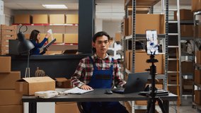 Asian worker recording ad video in storage room, using social media streaming platform to advertise small business in warehouse. Group of people doing teamwork for online promotion.