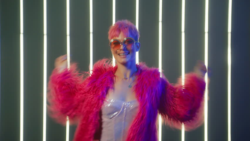 Young Girl with bright pink hair raising and waving arms in dancing moves. People Energy celebrating New Year Slow Motion. Happy Laughter Trendy Female Listen Music and Dance in Night club neon lights