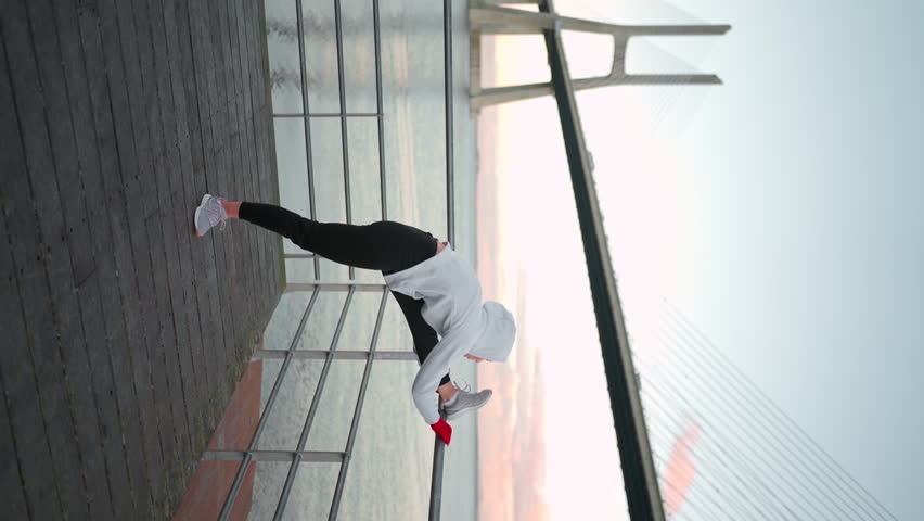Middle age woman stretching legs before kickboxing exercises. Caucasian athletic female does lunges exercises stretch leg seaside view with bridge and blue sky background. Vertical footage | Shutterstock HD Video #1100493749