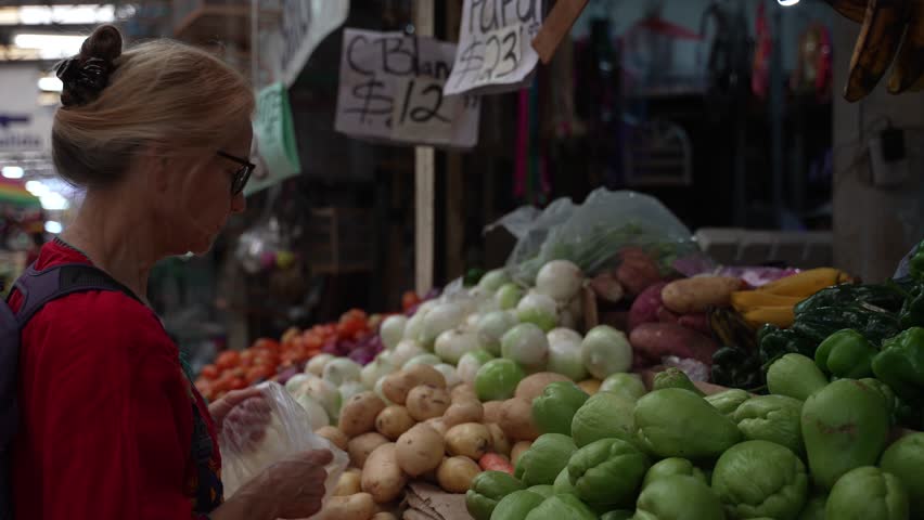 Attractive blonde mature senior woman carrots, vegetables and fruit at a local indoor market in Mexico. | Shutterstock HD Video #1100494703
