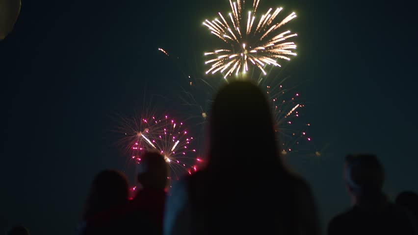 People on the holiday look at the fireworks in the night sky and at the big inflatable airship. Back view Royalty-Free Stock Footage #1100495251