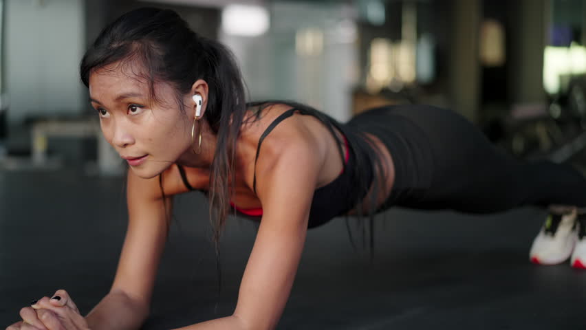 Attractive young asian woman doing elbow plank holds at the gym. Fit girl training at fitness center | Shutterstock HD Video #1100495581